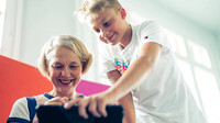 Mutter und Sohn testen gemeinsam das KatzeQ-Spiel auf einem Tablet in entspannter Umgebung.